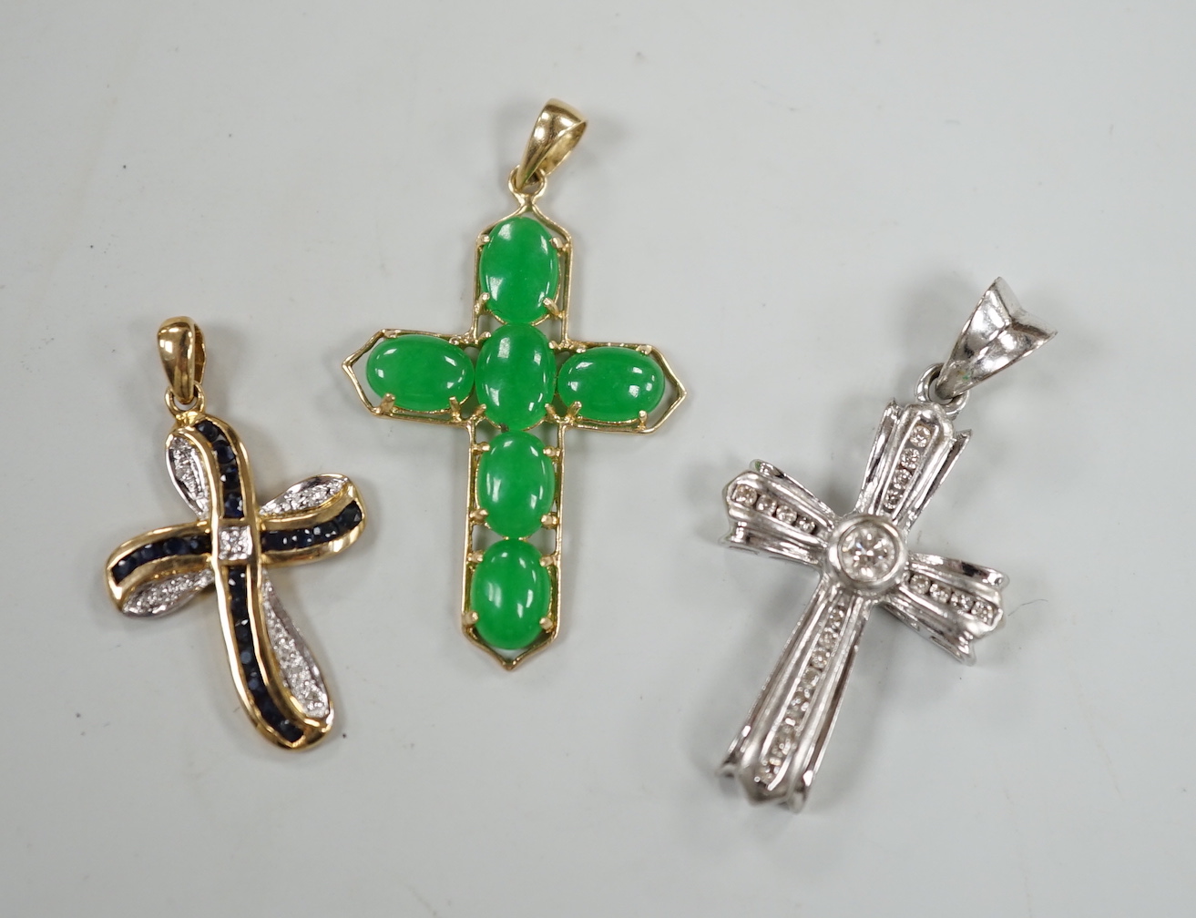 A modern 9ct white gold and diamond cluster set cross pendant, 27mm, a modern 9ct gold, sapphire and diamond chip set cross pendant, gross 7.4 grams and a 14ct gold and six stone cabochon jade set cross pendant, gross we